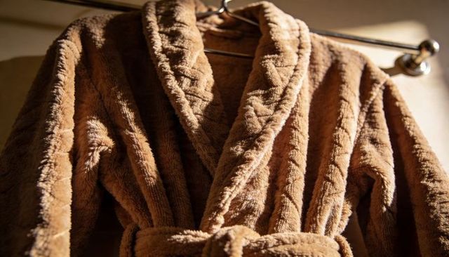 Plush brown bathrobe hanging on chrome bar, soft textured fabric and warm lighting