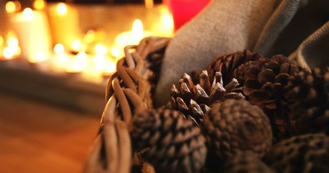 This image showcases pine cones arranged in a wicker basket illuminated by warm candlelight in the background. Suitable for illustrating cozy home decor, holiday preparation, autumn atmosphere, and natural elements in interior design. Perfect for seasonal blogs, social media posts, and ads promoting holiday decorations and cozy home products.