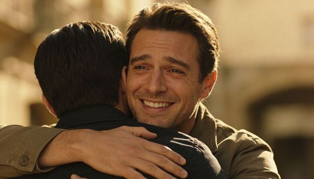 Tearful reunion hug between two men on sunlit narrow street with warm golden light