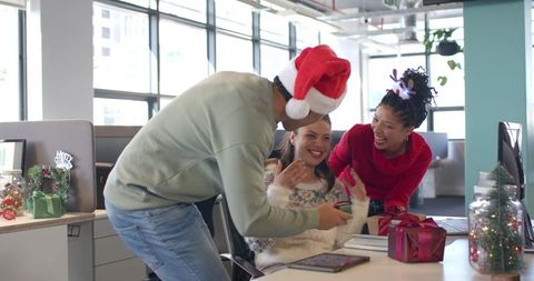 Multicultural coworkers celebrating holiday at office desk with santa hat and gifts