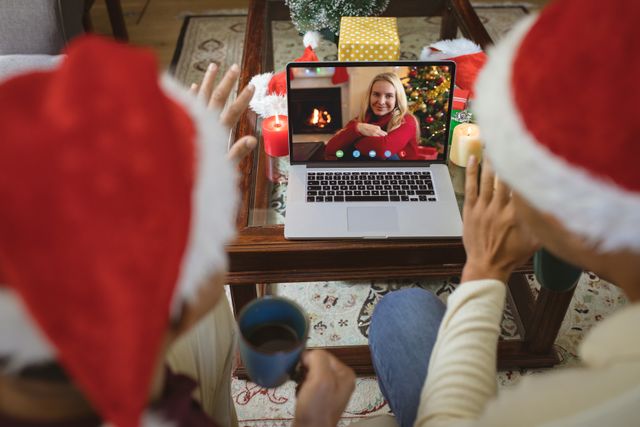 Couple in Santa hats engaged in a joyful video call with a friend during Christmas. Perfect for illustrating themes of holiday celebrations, virtual gatherings, and staying connected with loved ones through technology. Can be used in articles, marketing materials, or social media content highlighting modern holiday traditions and remote interactions.