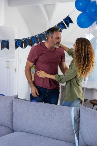 Mature couple embracing and celebrating birthday at home with balloons and banner