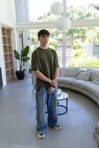 Teenage male standing in minimalist living room with large windows, garden view and natural light