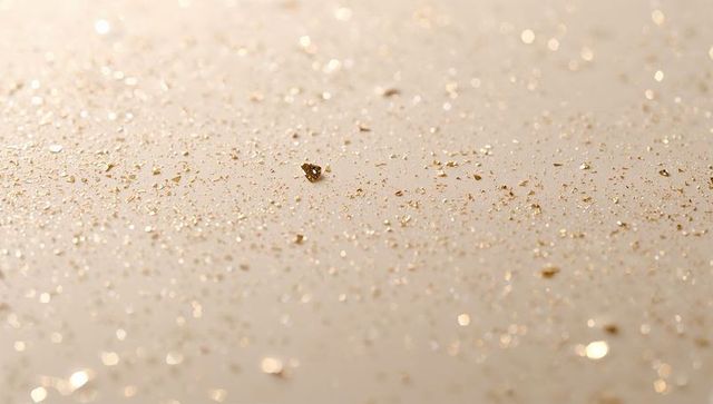 Single gold flake on cream surface with glittering bokeh and warm macro texture