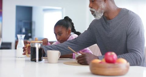African american grandfather and granddaughter making coffee together at kitchen island