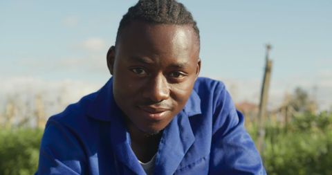 Young Farmer Smiling Amidst Lush Field in Blue Overalls