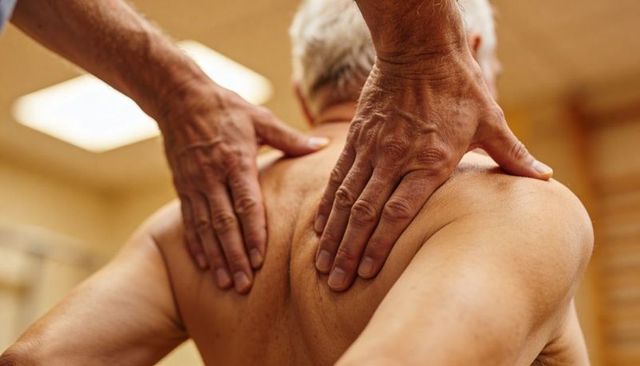 Therapist kneading senior back and shoulders during physiotherapy session for pain relief