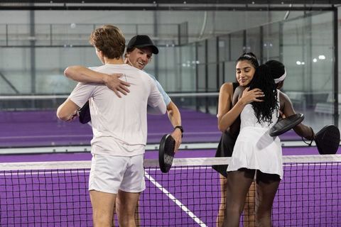Mixed-gender padel players hugging at net on vibrant purple court after match