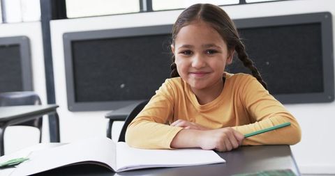 Young student smiling in classroom holding pencil