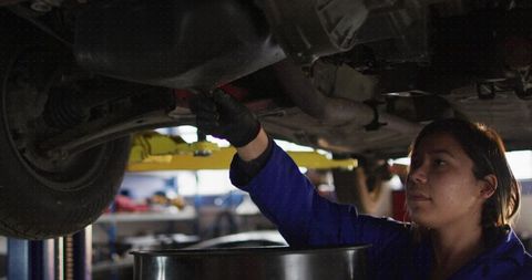 Skilled female mechanic draining oil in busy workshop environment