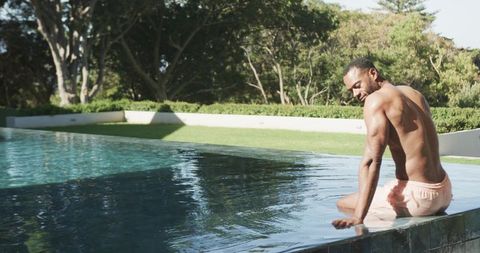 Man sitting on infinity pool edge dipping hand into water making ripples for wellness