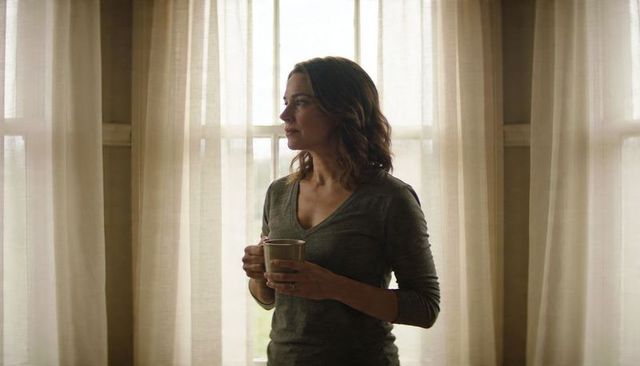 Woman holding mug gazing through sheer curtains morning light minimalist neutral interior