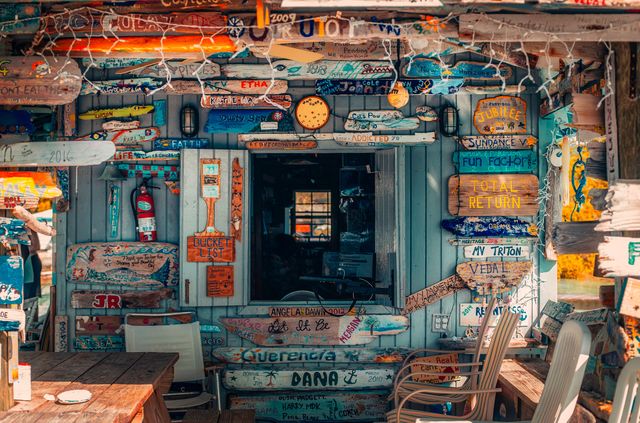 Playful and eclectic exterior of a beach café adorned with a variety of colorful wooden signs capturing seaside charm. Ideal for travel brochures, vacation blogs, and hospitality marketing to evoke a sense of summer fun and creativity.