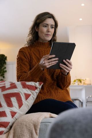 Woman reading tablet on sofa wearing rust sweater in cozy modern living room