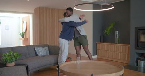 Warm hug between diverse male friends in modern cozy living room with wood slat wall