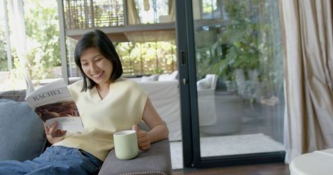 Woman Relaxing on Couch with Book and Mug in Bright Living Room