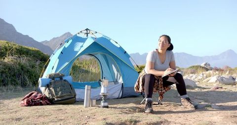Woman Journaling by Mountain Tent on Scenic Camping Adventure