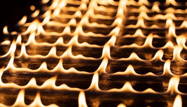 Flickering golden flames forming repeating wavy grid on ridged metal burner surface