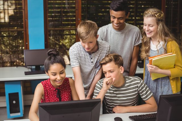 Group of students smiling while working on a computer project in a classroom, showing collaborative learning and teamwork. Useful for educational content, school websites, and articles about technology in education.
