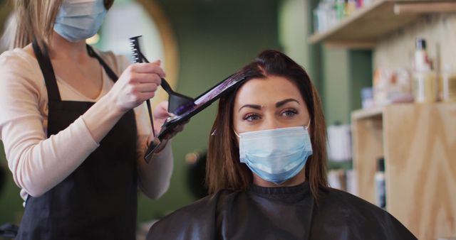 Hairdresser applying dye to woman's hair in salon, both wearing masks - Download Free Stock Photos Pikwizard.com
