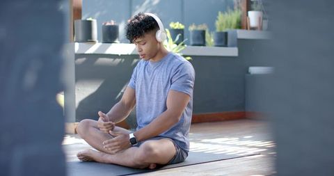 African american man meditating on sunlit balcony wearing headphones and smartwatch