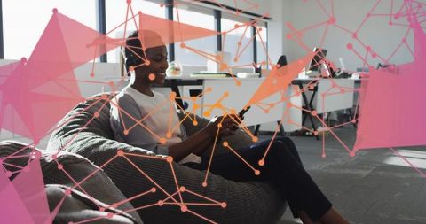 Mid-adult woman relaxing on beanbag using tablet in modern connected office workspace