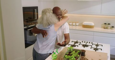 Diverse couple hugging in kitchen while tending seedlings