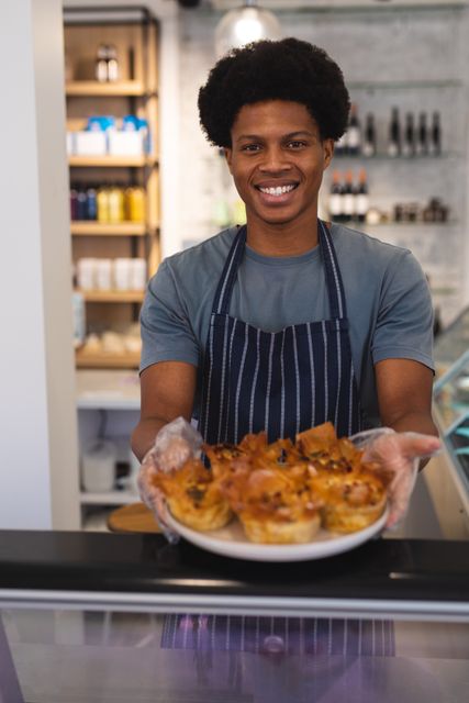 Portrait of smiling african american young male owner serving food at cafe. unaltered, cafeteria, barista, occupation, temptation, food and small business concept.