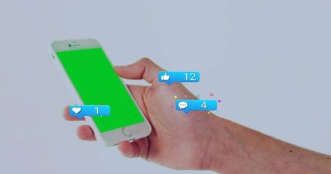 Right hand holding smartphone with green screen and floating social notification bubbles