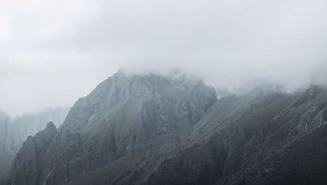 Jagged alpine ridge rising through clouds and fog over scree slopes, moody landscape