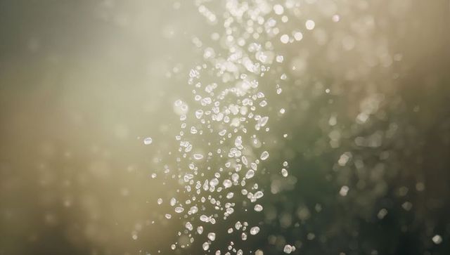 Backlit water droplets streaming into sparkling mist with soft bokeh background