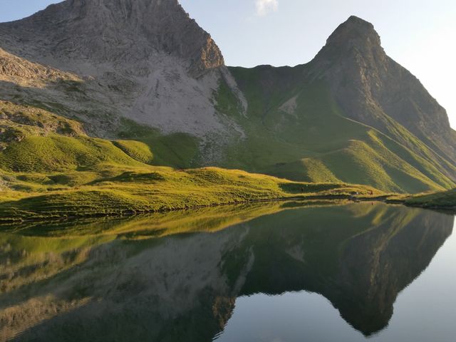 Serene lake reflecting surrounding mountains under early morning light. Ideal for travel, nature blogs, environmental publications, desktop backgrounds, and advertisements promoting tranquility and outdoor activities.