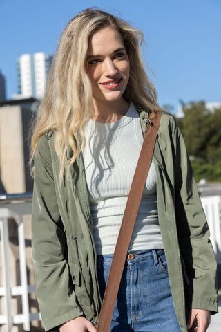 Young woman standing on rooftop balcony wearing olive jacket and jeans, urban street style