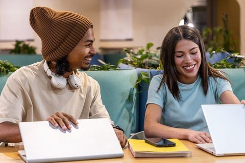 Young diverse professionals collaborating on laptops in modern coworking cafe