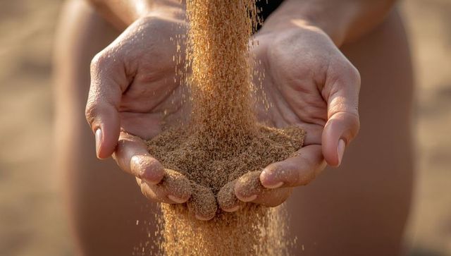 Cupped hands letting golden sand pour through fingers on sunlit beach closeup