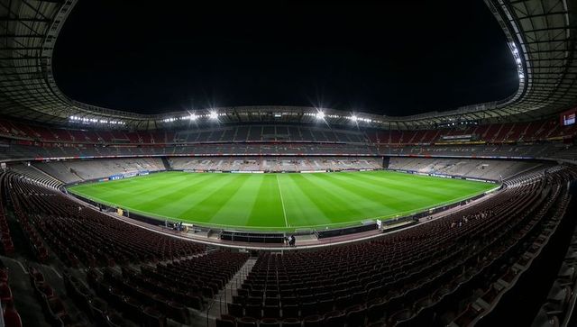 Floodlit empty football stadium at night showing pristine green pitch and tiered seating