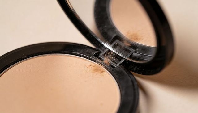 Black compact face powder with mirror showing scattered loose particles on vanity closeup