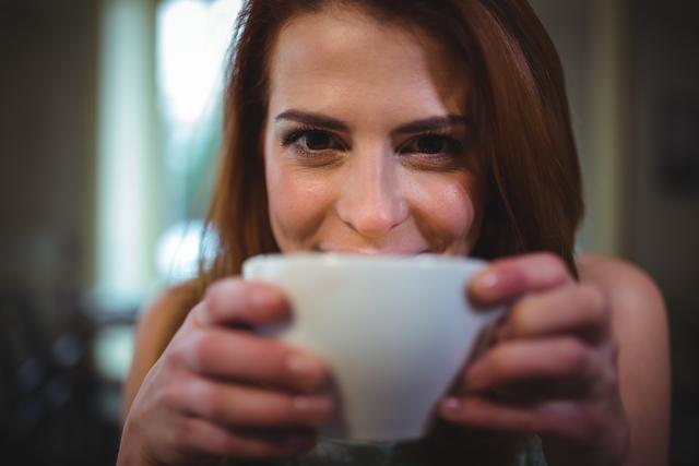 This close-up shot of a woman enjoying a cup of coffee at a cafe captures a moment of relaxation and contentment. Perfect for use in marketing materials for coffee shops, lifestyle blogs, and advertisements promoting relaxation and leisure activities.