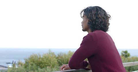 Leaning on railing and gazing across ocean horizon at coastal overlook during overcast day