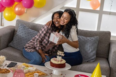 Young diverse friends exchanging gift and celebrating birthday on cozy living room sofa