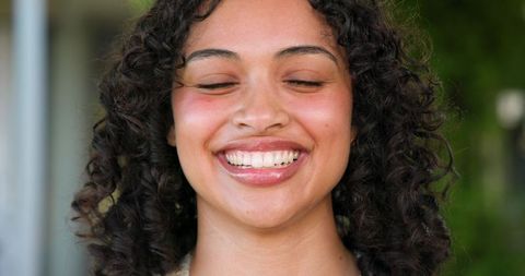 Joyful Woman with Curly Hair Smiling in Sunlight