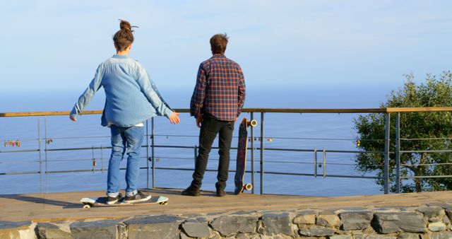 Image depicts two individuals engaging in skateboarding on a wooden deck with a stunning ocean view. Useful for concepts involving outdoor activities, leisure, travel adventure, friendship, and relaxation. Perfect for travel blogs, outdoor activity promotions, and lifestyle content.