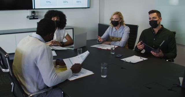 Diverse group of business colleagues wearing masks in discussion in meeting room. working in a modern office during covid 19 coronavirus pandemic.