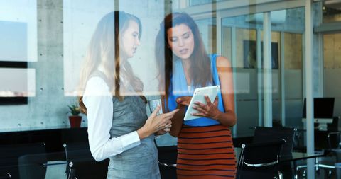 Businesswomen Engaged in Discussion Over Tablet in Office