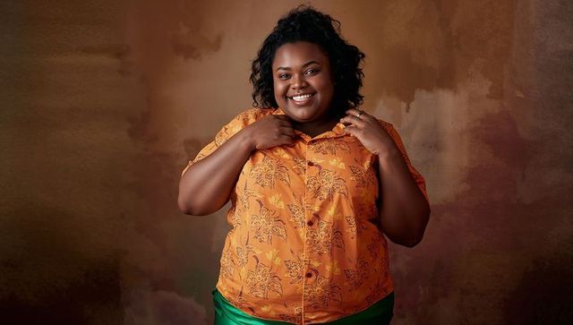 Confident smiling black plus-size woman wearing orange floral shirt and green skirt posing