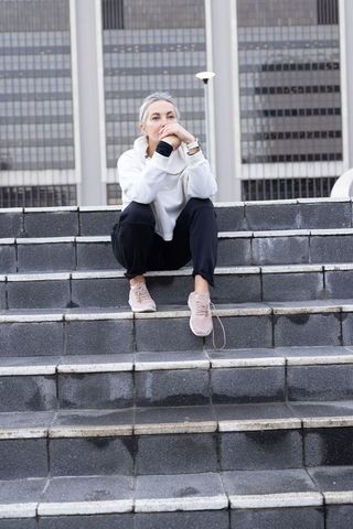 Pensive mature woman sitting on urban steps after rain, resting and gazing