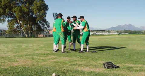 Green Uniform Baseball Team Celebrating Huddle on Sunny Outfield with Mountain Backdrop