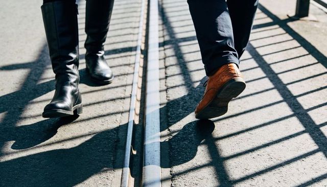 Contrasting footwear walking along tram tracks with railing shadows and sunlit pavement