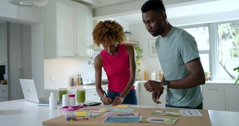 Black couple planning home vision board on corkboard in sunlit modern kitchen workspace