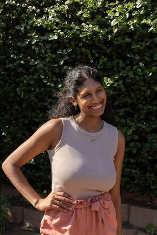 African american woman smiling, posing in sunlit garden wearing salmon shorts, beige tank